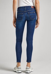 Jeans ajustados de color azul oscuro, fabricados en denim, con dos bolsillos traseros que presentan costuras en contraste y una etiqueta de cuero marrón en la cintura.