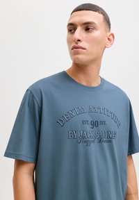 Blue cotton t-shirt with short sleeves, featuring a printed design in dark blue text that reads "DENIM ATTITUDE" and brand details.