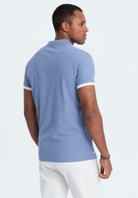 Modrá polo košile s bílým lemováním na límci a rukávech. Slim fit, krátké rukávy a hladká textura. Žádné viditelné vzory ani loga.