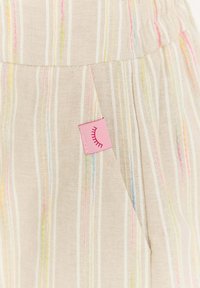 Béžová tkanina s vertikálnymi pastelovými pruhmi a prišitým ružovým štítkom s dizajnom zatvorených rias blízko švu vrecka.