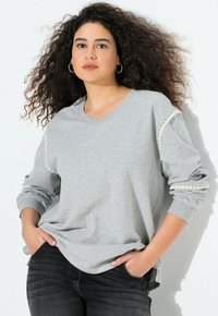 Světle šedá mikina s dlouhými rukávy a výstřihem do V, s dekorativním prošíváním podél rukávů. Měkký materiál a volný střih.