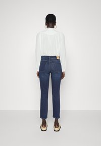 Tmavě modré džíny s vysokým pasem a rovnými nohavicemi, kombinované s bílou halenkou se sklady na výstřihu a dlouhými rukávy.