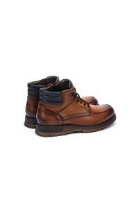 Bottes brunes en cuir au niveau des chevilles avec des accents noirs, bout rond, design à lacets, col rembourré et semelle en caoutchouc texturée pour une meilleure adhérence.