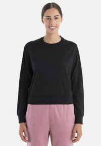 Sudadera negra corta con cuello redondo y mangas largas, que presenta puños de canalé. Textura suave, combinada con pantalones rosa claro.