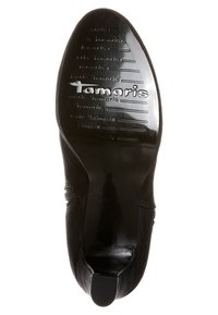 Chaussure noire avec une tige en daim doux et une semelle en caoutchouc lisse et brillante. Présente des motifs en relief et le logo "Tamaris" au bas.