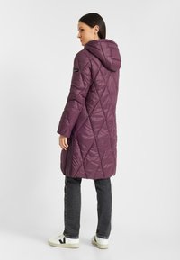 Paarse, gewatteerde jas met kap en een middellange snit, ruitpatroon en zijzakken. Gecombineerd met donkere jeans en witte sneakers.