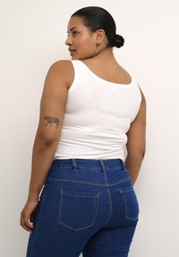 Top bianco a canotta con spalline larghe abbinato a jeans in denim blu a vita alta con tasche posteriori e dettagli di cucitura visibili.