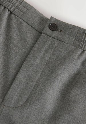 Szare dostosowane spodnie z płaskim przodem, zapięciem na guzik i fakturą przypominającą finezyjną wełnę. Posiadają delikatne przeszycia w pasie oraz kieszenie.