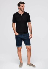 Black short-sleeve collared knit shirt with vertical texture; paired with cuffed dark denim shorts; light gray casual shoes.