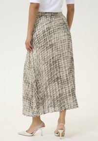 Falda midi plisada en un color neutro claro con un patrón abstracto gris. Cintura elástica y textura fluida. Llevada con zapatos de tacón plateados.