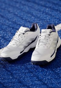 Weiße Sportschuhe mit atmungsaktivem Mesh-Obermaterial, navyblauen Akzenten, gemustertem Texturdesign und einer Gummilaufsohle für guten Grip.