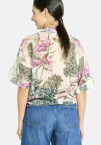Floral blouse in sheer fabric, featuring pink lilies and green accents. Short sleeves, relaxed fit, and round neckline.