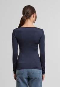 Granatowa koszula z długim rękawem o dopasowanej sylwetce i szerokim dekolcie, wykonana z gładkiego materiału, zestawiona z jasnoniebieskimi spodniami typu cargo.