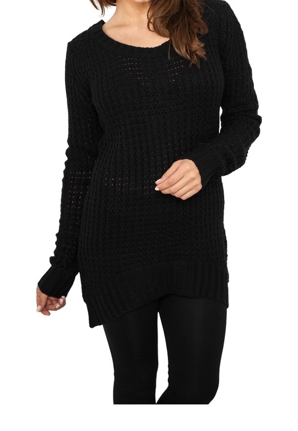 Femme portant un long pull en tricot noir avec un ourlet asymétrique et des leggings noirs, posant une main près de sa taille.