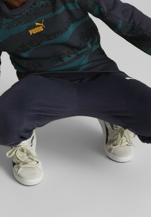 Sportieve outfit met een marineblauwe sweatshirt met groene strepen en een Puma-logo, gecombineerd met marineblauwe joggingbroek en crèmekleurige sneakers.