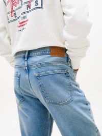 Jeans de mezclilla azul claro con corte recto, con bolsillos traseros y una etiqueta de cuero marrón en la cintura.
