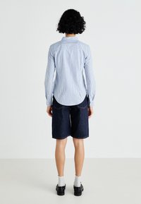 Μπλε και λευκή ριγέ μπλούζα με μακριά μανίκια, συνδυασμένη με σκούρα τζιν σορτς, με καμπύλη ακμή και πίσω τσέπες. Συνδυασμένο με γκρι κάλτσες και παπούτσια.