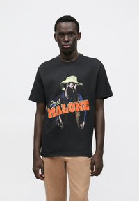 Black cotton t-shirt featuring a colorful graphic of a man in a cowboy hat with the text "Post MALONE." Short sleeves and relaxed fit.