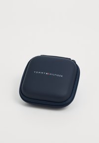 Carcasă dură de culoare albastru închis cu o finisare uniformă, având închidere cu fermoar și logo-ul imprimat alb "TOMMY HILFIGER" pe partea de sus.