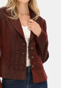 Burgundzka kurtka z usztywnionym kołnierzem, teksturowanymi falbanami z przodu i dwoma dekoracyjnymi guzikami. Tkanina jest lekka i teksturowana.