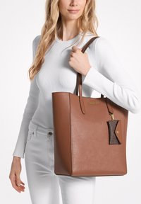 Borsa a tracolla marrone con forma strutturata, materiale sintetico liscio e manici lunghi. Presenta un piccolo portachiavi in pelle marrone in contrasto.