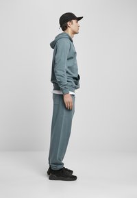 Felpa azzurra chiara e pantaloni tuta coordinati, caratterizzati da una vestibilità rilassata e polsini elasticizzati, abbinati a sneakers nere e un cappellino.