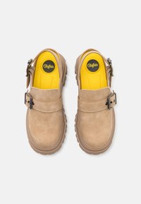 Pantofi slip-on bej cu un superior din piele texturată, cataramă metalică ajustabilă și branturi căptușite galbene. Talpa din cauciuc masiv cu aderență.