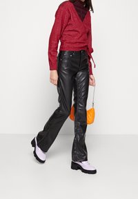 Roter Pullover mit Metallic-Effekt, schwarze Leder-Hose mit Schlag, lavendelfarbene Chunky-Loafer und eine kleine orange gestepptte Handtasche.