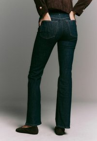 Mørke denim flared jeans med baglomme, kontrasterende syninger og en glat tekstur, parret med brune flade sko.