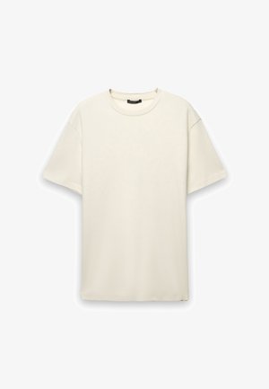 T-shirt di cotone color crema con vestibilità comoda, maniche corte e scollatura rotonda. Tessuto liscio senza motivi o dettagli visibili.