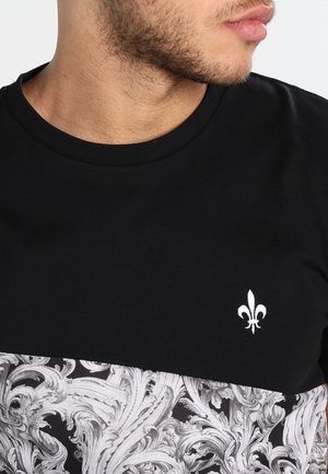 Maglietta nera con logo bianco a fiordaliso sul petto e motivo decorativo a vortici in bianco e nero lungo la metà inferiore.