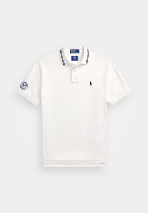 Cămașă polo albă din bumbac cu dungi marine la guler. Prezintă un mic logo marin pe piept și un emblema pe mânecă.