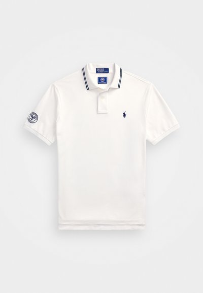 Biała koszulka polo z bawełny z granatowymi paskami na kołnierzyku. Posiada małe granatowe logo na klatce piersiowej oraz emblemat na rękawie.
