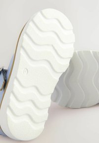 Scarpe casual con tomaia blu chiaro, suola in gomma bianca robusta con una texture ondulata e un accento marrone lungo il bordo della suola.