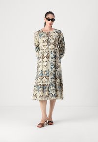 Μακριά κρεμ φόρεμα με μπλε και καφέ λουλουδάτα σχέδια. Διαθέτει λαιμόκοψη με κορδόνι, μακριά μανίκια και φούστα με επίπεδα. Συνδυάζεται με καφέ πέδιλα με τακούνι.