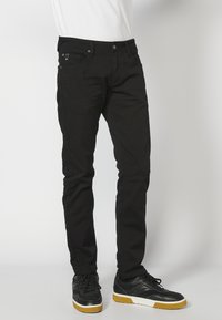 Fekete farmernadrág slim fit szabással, öt zsebből álló kialakítással és sima felülettel. Fekete sportcipővel párosítva, amely gumírozott talppal rendelkezik.