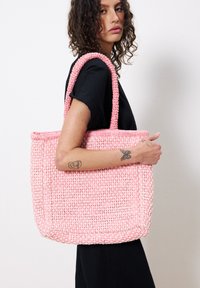 Roze geweven tas met twee handgemaakte handvatten, rechthoekige vorm, gestructureerd oppervlak en een stevige bodem. Geschikt voor casual gebruik.