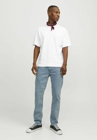 Tricou alb din bumbac, cu o croială relaxată, asociat cu blugi decolorati, de un albastru deschis. Accesoriile includ o bentiță roșie legată la gât și adidași negri.