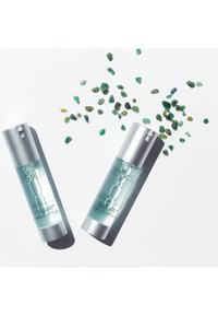 Due bottiglie trasparenti di concentrato detergente con tappi silver, posizionate su uno sfondo bianco. Gemme verdi sparse intorno.