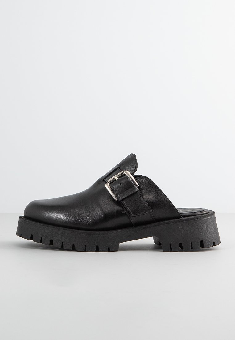 Sabot en cuir noir avec une large sangle et un accent de boucle en argent, doté d'une épaisse semelle en caoutchouc crantée pour une traction et une durabilité accrues.