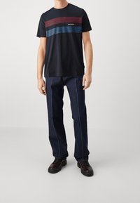 Camiseta de marinero con rayas horizontales rojas y azules, combinada con jeans de mezclilla oscura con costuras en contraste y zapatos negros con cordones.