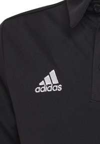 Schwarzpoloshirt aus glattem Stoff mit Kragen und einem Knopf. Zeigt ein weißes gesticktes Adidas-Logo auf der linken Brust.