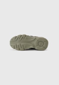 Suola di sneaker in gomma verde con un motivo di battistrada testurizzato e forme arrotondate, caratterizzata da scanalature robuste e un dettaglio di logo circolare.
