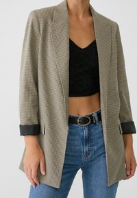 Blazer med hundtandmönster i beige och svart, med en strukturerad design, slagkrage och uppvikta ärmar. Matchas med blå högmidjade jeans.