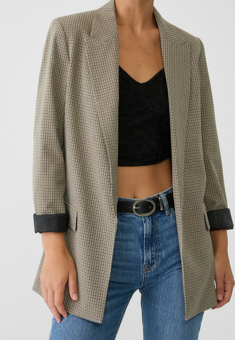 Blazer med hundtandmönster i beige och svart, med en strukturerad design, slagkrage och uppvikta ärmar. Matchas med blå högmidjade jeans.