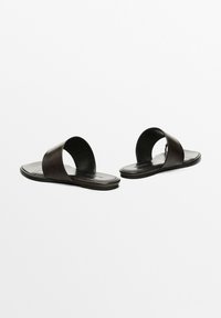 Černé kožené skluzné sandály se širokým páskem přes nohu, plochou podrážkou a hladkým povrchem. Minimalistický design bez viditelného kovového vybavení.