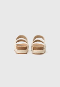 Les sandales espadrilles beiges sont dotées de quatre larges brides, d'un dessus en tressage, d'une semelle intérieure en liège naturel et d'un intermédiaire recouvert de jute, avec une semelle extérieure en caoutchouc plate.