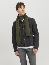 Sciarpa di lana di colore verde oliva avvolta attorno al collo, abbinata a una giacca di denim nera e jeans grigi. Design semplice e texturizzato.