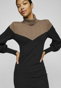Abito lavorato a maglia con colletto alto marrone e corpo nero, decorato con un motivo a zigzag sul petto, maniche lunghe e polsini a costine.