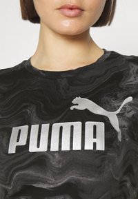 Camisa negra de manga corta con un patrón en espiral, gran logo plateado de "PUMA" y la silueta de un puma saltando en plateado en el pecho.